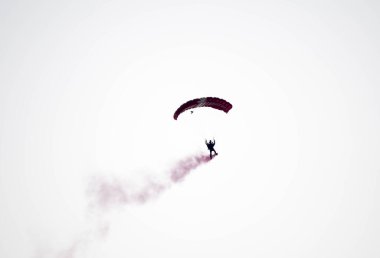 silhouette parachute stunt unfocused and blurry while gliding in the air with red smoke trail during an air exhibition