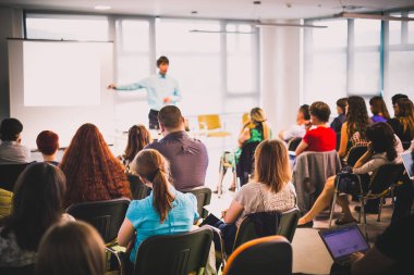 İş toplantısında konferans salonunda konuşma yapan konuşmacı. Konferans salonundaki tanınmayan seyircilerin arka görüntüsü.
