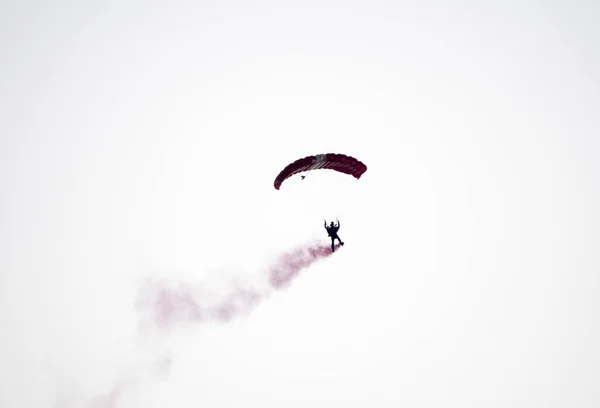 空中展示中に赤い煙道で空中を滑走しながら シルエットパラシュートのスタントが集中せずぼやけている — ストック写真