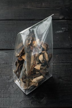 Siyah ahşap masa arkasında, plastik bir paketin içinde, doğranmış, kurutulmuş yabani mantar karışımı.