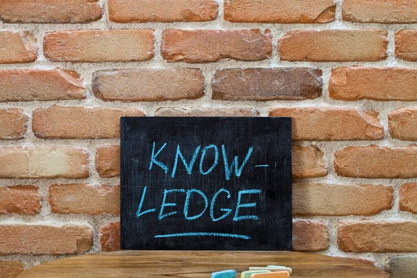 粉笔写字板上写着 Knowledge 的字样 粉笔用手浸 粉笔画在砖墙背景的木制桌子上 — 图库照片