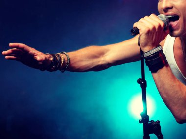Şarkıcı konser sahnesinde mikrofonla şarkı söylüyor.
