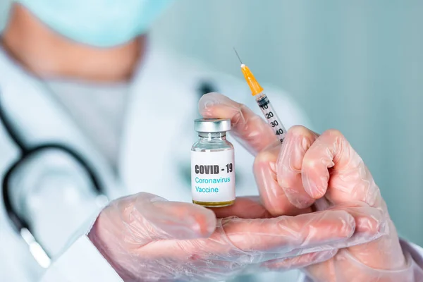 医師または看護師の制服と手袋顔マスク保護を身に着けている研究室で薬を保持バイアルワクチンボトルでCovid 19コロノウイルスワクチンラベル — ストック写真