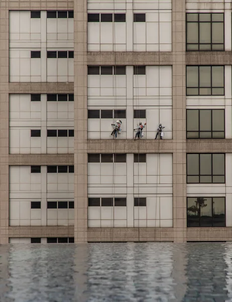 高层办公大楼设有倒影式游泳池的工人清洗窗户组 — 图库照片