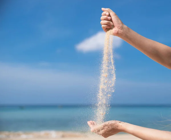 Woman pouring the sand from hand to hand on the beach, blue sky.