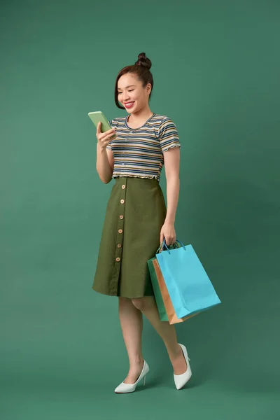 緑の背景でスマホでおしゃべりしながら買い物袋を持った陽気でエレガントな女の子 — ストック写真