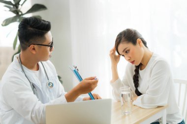 Üniformalı genç Asyalı doktor ve beyaz önlüklü hasta ile birlikte çalışıyor.