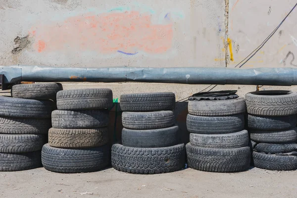 许多破旧的汽车轮胎堆在垃圾场的墙上 — 图库照片