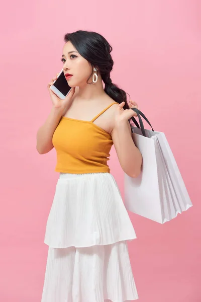 魅力的な女性は 携帯電話を使用し ピンクの背景にいくつかのショッピングバッグを運ぶ — ストック写真