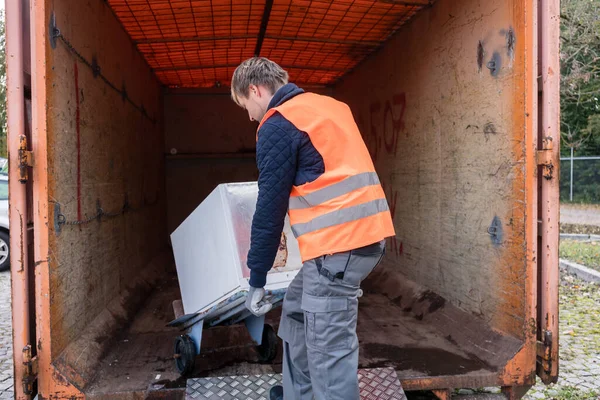 Man putting old washing machine in container