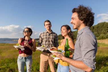Doğadaki barbekü partisindeki arkadaşlar bira içip hamburger yiyorlar.