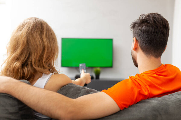 "Пара смотрит телевизор с зеленым экраном. Девушка нажав пульт управления."