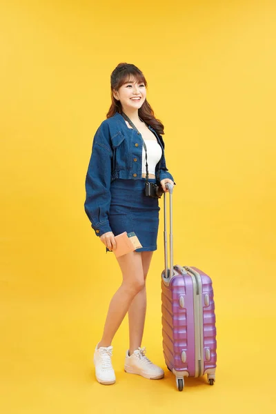 旅行的概念 带着黄色背景的手提箱和护照的快乐女人 — 图库照片