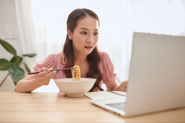 Muotokuva Nuori Aasialainen Tyttö Käyttää Kannettavaa Tietokonetta Syödessään Nuudeleita Kotona — kuvapankkivalokuva