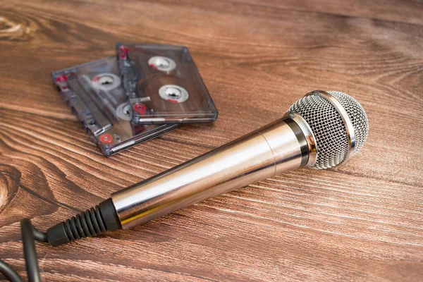A silver analog microphone sits next to old cassette tapes