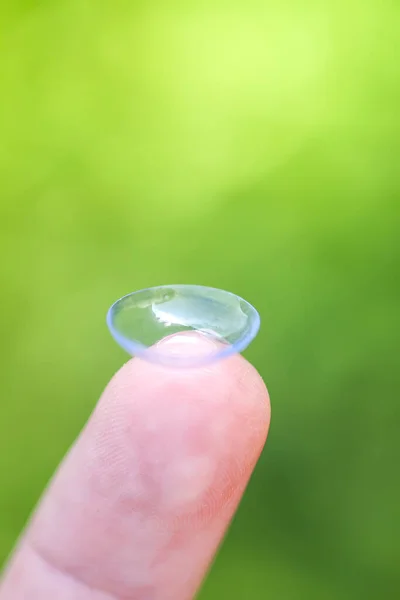 Transparent contact lens on finger tip on blurred green summer nature background