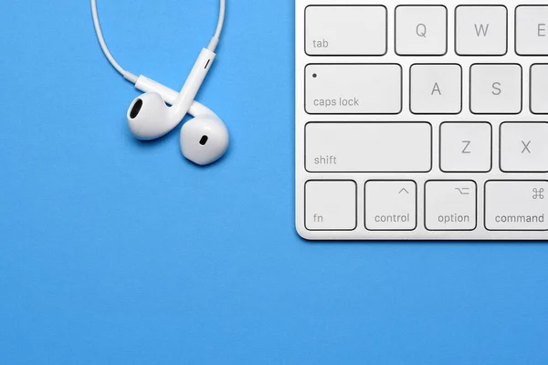 Computer Keyboard and headphones on blue with copy space.