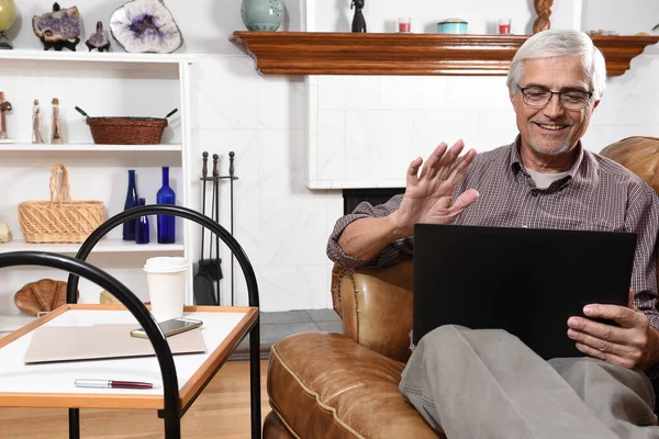 由于Covid 19的流行 老年人在家中与家人视频聊天时 一边在笔记本电脑屏幕前挥手 — 图库照片