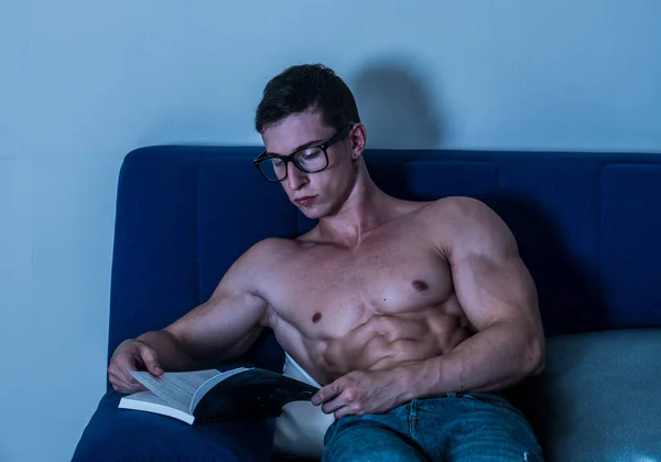 年轻的男性健美运动员坐在沙发上看书 — 图库照片