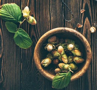 Cuisine photo of fresh hazelnuts with leaves in bowl on wooden table