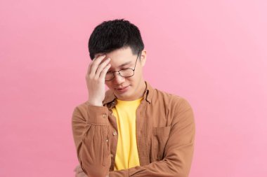 Young disappointed man holding his head isolated on pink background
