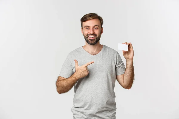 Gri Tişörtlü Yakışıklı Sakallı Adamın Portresi Kredi Kartını Gösteriyor Gülümsüyor — Stok fotoğraf