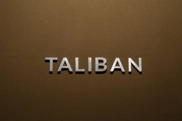 Wort Taliban Mit Silbernen Metallbuchstaben Auf Rauhbraunem Khakifarbenem Stoff — Stockfoto