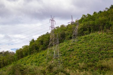 Gökyüzü ve dağ zeminli yüksek voltajlı elektrik pilonu ve iletim güç hattı görüntüsü