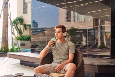 Asyalı adam kahve içiyor ve havuz başında müzik dinliyor.