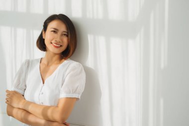 Genç ve güzel bir kadın duvarın önünde duruyor, güneş ışığı güzel bir şekilde düşüyor. Perdelerin gölgesi.