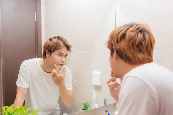 若い男は鏡の前で立っていると 彼の顔に触れる — ストック写真