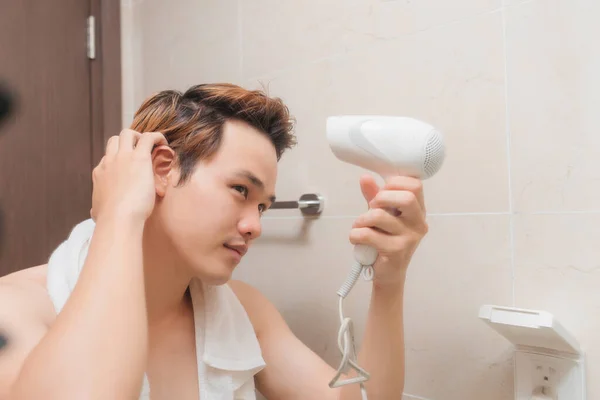 トレンディな若い男は浴室の鏡の前でブロードライヤーで彼の髪を乾燥させる — ストック写真