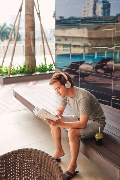 stock image man reading book in pool deck chair while listening music