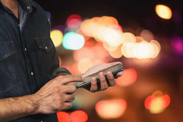 Человек Использующий Свой Мобильный Телефон Ночью Светлом Боке Фоне — стоковое фото