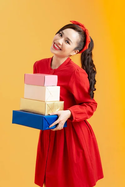 オレンジ色の背景に隔離された現在の箱のスタックを保持する赤いドレスのかわいい若い女の子の肖像画 — ストック写真