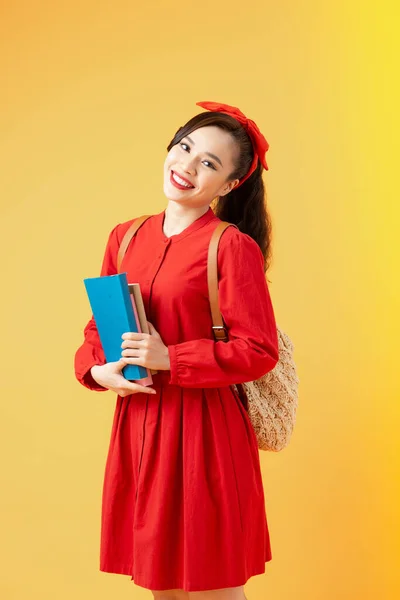 笑顔かわいいですアジアの女の子保持本とカメラを見て隔離された上にオレンジの背景 — ストック写真