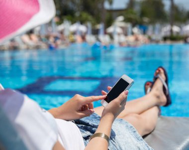 Güneş yatağında akıllı telefon kullanan kadın. 