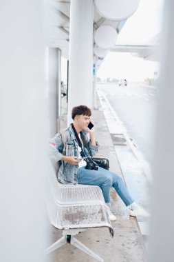 Havaalanındaki otobüs durağında cep telefonundaki gülen adamın yan portresi.