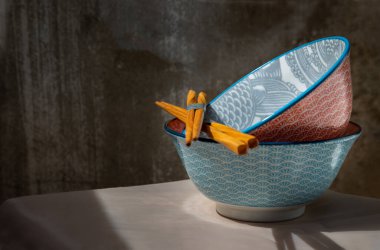 Two ceramics bowls with wooden chopsticks on pink table cloth.