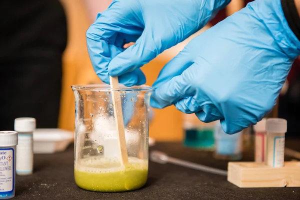 在学校实验室进行的科学实验中 莱蒂戴着手套的手倒了一大杯液体 — 图库照片