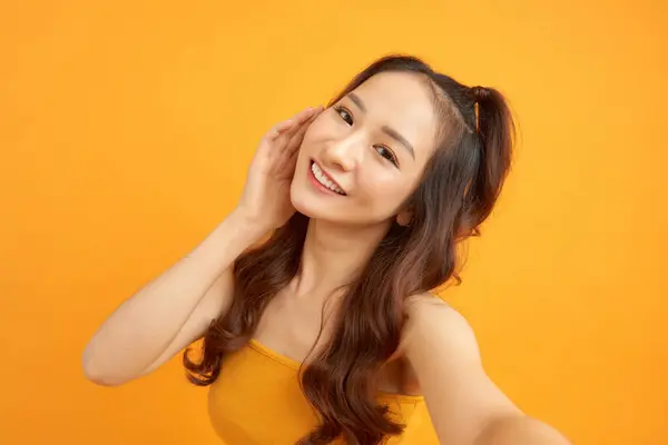黄色の背景に孤立したスマートフォンで自撮り写真を作る笑顔のかわいい女性の肖像画 — ストック写真