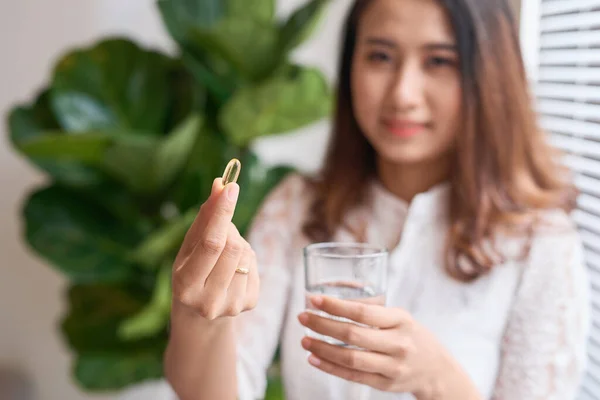 side view of beautiful woman taking vitamin capsule with a glass of water isolated in white