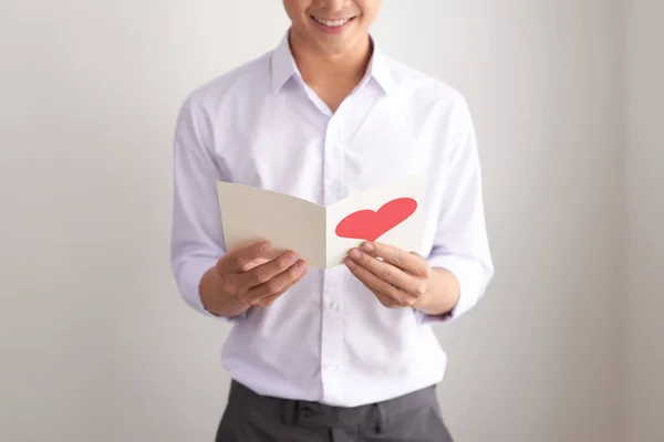 若いですハンサムなアジア人男性読みますグリーティングカードとともにハート形上の白い背景 — ストック写真