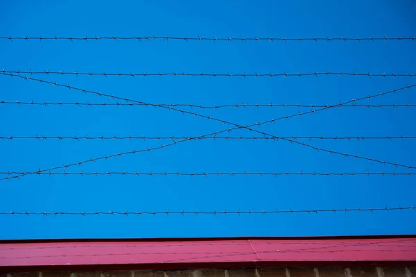 青い空に対する刑務所のフェンスに有刺鉄線 — ストック写真