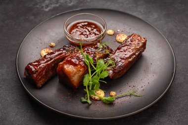 Soslu ızgara pirzola ve siyah bir tabakta otlar.