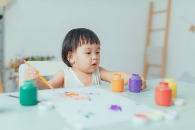 Beyaz masaya boya ve fırçayla çizim yapan çocuk