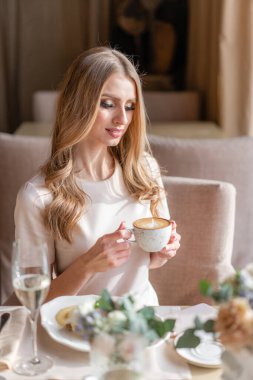 Nice woman eat breakfast in cafe. Portrait of young charming female drinking coffee and toasted sandwich in modern coffee shop.