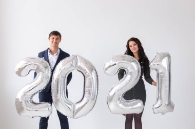 Yeni yıl, kutlama ve tatil konsepti - beyaz arka planda yeni yıl için gümüş balonlardan yapılmış 2021 tabelasıyla eğlenen aşk çifti