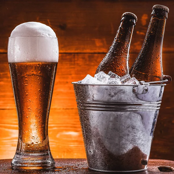 氷の入ったバケツに2本のビールと濃い背景の隣に緑豊かな泡のビール — ストック写真