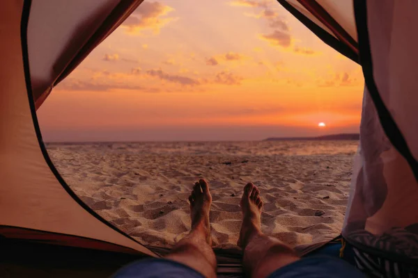 stock image Man resting in a tent on beach at sunset.